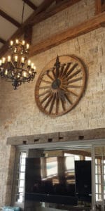 Large wooden wagon wheel clock in stone wall